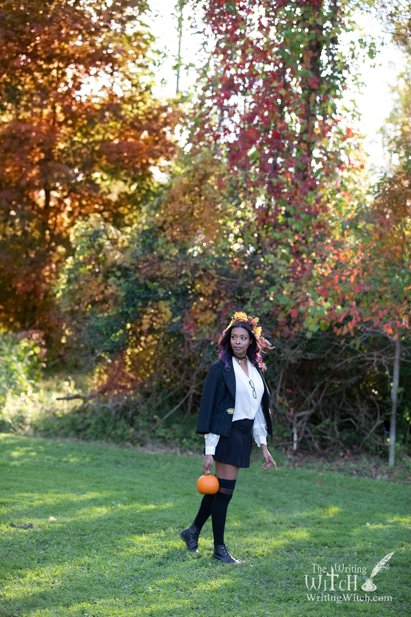 Modern witch outdoors with pumpkin and Autumn leaves.